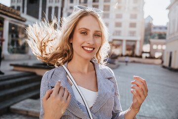 Wonderful european woman with blonde hair spending leisure time in city. Outdoor photo of elegant excited girl.