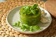 Italian green pesto sauce with leaf of basil on top in clear glass jar on a plate. 