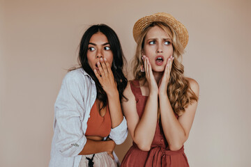 Emotional girl with curly hairstyle standing on brown background. Worried lady in canotier posing with friend.