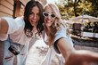 © Look! - Fashionable latin girl making selfie with friend. Outdoor portrait of two cute ladies having fun together.