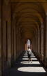 Woman in hat standing in portico with shadows and looking back
