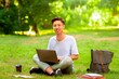 © Prostock-studio - Smiling asian student guy sitting with laptop outdoors, preparing for exams