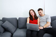 © cocorattanakorn - Young Caucasian couple love relaxing and smiling with laptop in social media for shopping online in living room. Technology for Married family lifestyle on holiday Concept.