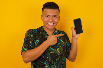 Excited man standing against yellow background pointing with finger at digital device. Studio shot of shocked guy holding smartphone with blank screen. Advertisement concept.