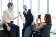 © cocorattanakorn - Smiling young Asian and Senior Caucasian businesspeople teamwork relaxing and holding a mug of hot coffee for take a photo with smartphone at modern office. Business and lifstyle concept