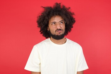 Gloomy, wondering young man face looking up lips together, being upset thinking about something important, keeps hands down, man standing indoors.