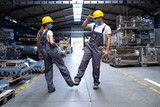 Fototapeta  - Workers wearing uniforms and hardhat at factory touching with legs and greeting due to corona virus and infection.