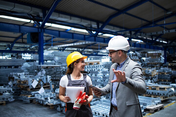 Manager wearing hardhat and industrial worker discussing about production in metal factory. Positive people talking about business.