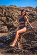© unai - Lifestyle, Caucasian brunette in a luxurious black swimsuit with sparkles enjoying the summer at sea. Portrait of pretty young woman sitting on the rock in summer
