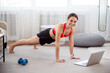 © Admiral - Sporty woman doing plank exercise and watching online workout session on laptop, training in living room
