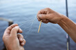 Faceless male untangles knot of fishing line over water on background, unknown person holding fishing line with bobber in hands, man catching fish with rod.