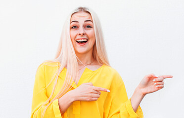 Advertisement concept. Positive, pretty woman with beaming smile in yellow shirt on white background is pointing with her two index finger and looking on empty copy space