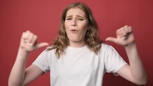 Portrait Of Dissatisfied Girl Showing Thumbs Down, Disapproval Sign, Gesturing Dislike To Bad Service, Disagree With Suggestion, Isolated On Red Background.