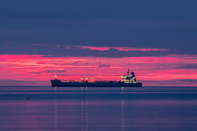A Long Empty Cargo Trailer Ship With No Containers On A Calm Sea During A Beautiful Red And Blue Sunset
