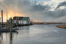 Nautical Scene With A Bait House, Pilings, A Dock And A Small Boat At Sunset.
