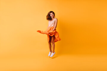 Canvas Print - Full-length portrait of debonair stylish lady jumping in studio. Gorgeous ginger girl in orange skirt having fun.