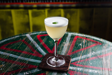 Wall Mural - A classic yellow sour cocktail with foam in a nick and nora glass with lime zest garnish