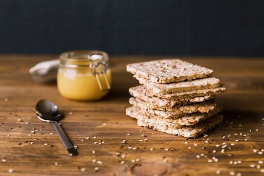 Stack of crusty crispbread on a brown wooden background in close up. Delicious substitute for bread. Healthy dietary product. Glass jar with honey and a spoon.
