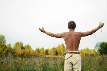 man stands with his arms outstretched against the sky stripped to the waist