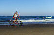 © Juan - joven montado en bici en la playa sonriendo y una lancha de fondo
