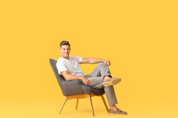 Young man relaxing in armchair against color background