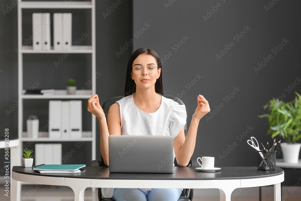 Young woman meditating at workplace in office
