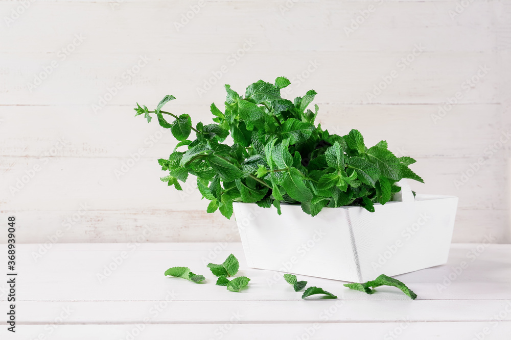 Fresh green mint in basket on white wooden background
