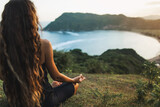 Fototapeta  - Woman meditating yoga alone at sunrise mountains. View from behind. Travel Lifestyle spiritual relaxation concept. Harmony with nature.