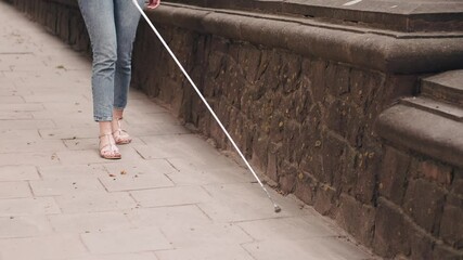 Wall Mural - Blind woman is walking on the sidewalk in city. Woman using a white cane.