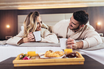 Smiling couple having breakfast in bed in hotel room