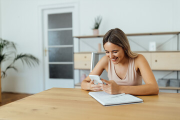 Wall Mural - Portrait of a happy young woman using smart phone, indoors.