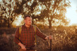 © honey_inside - Irish looking red bearded hunter in checkered shirt staying outdoors in the sunset light and holding his gun
