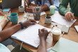 © Seventyfour - Close up of multi-ethnic group of people working together at cluttered table with cups, mugs and stationary items, teamworking or studying concept, copy space