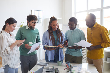 Wall Mural - Portrait of contemporary multi-ethnic business team standing around table in office and listening to female African-American leader giving instructions, copy space