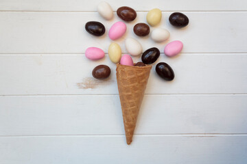 Wall Mural - Top view of ice cream cone with sweet almond eggs on white wooden table