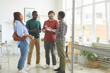 Full length portrait of multi-ethnic group of people dressed in casual wear and smiling cheerfully while discussing work standing in office