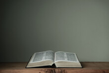 Open Holy Bible On A Red Wooden Table And White Wall Background. Religion Concept.
