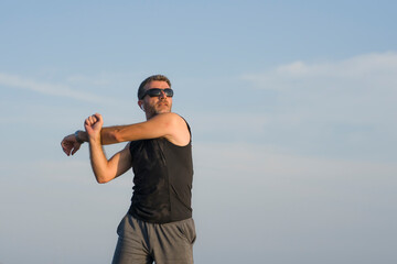 jogging Summer workout - young attractive and fit runner man training on beautiful beach stretching arms before running by the sea in fitness concept