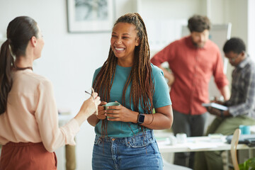 Wall Mural - waist up portrait of contemporary african-american woman smiling cheerfully while talking to female 