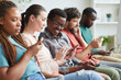 © Seventyfour - Portrait of multi-ethnic group of people sitting in row and using smartphones while waiting for conference, focus on smiling African-American man talking to female colleague beside him, copy space