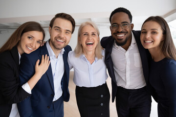 Poster - Middle-aged boss company staff members hugging standing together in office laughing looking at camera. Photo shoot corporate album, having gun enjoy friendly relations feels successful and confident