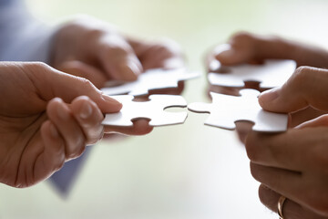 Close up hands of four businesspeople hold pieces of white puzzle, assemble jigsaw, put it together, joint path to problem solution, find way out exit of difficult situation. Support, teamwork concept