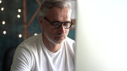 Canvas Print - Senior freelancer using computer working from office. Smiling grey-haired man in glasses typing on computer.