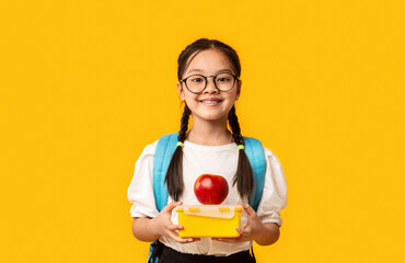 Smiling Chinese Schoolgirl Holding Lunch Box Posing On Yellow Background