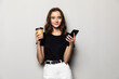 © dianagrytsku - Portrait of a young smiling girl in shirt texting message on mobile phone and holding cup of coffee to go over gray background