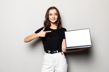 Portrait of a smiling woman pointing finger on blank laptop screen over gray background