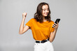 © dianagrytsku - Portrait of a satisfied young woman holding mobile phone and celebrating isolated over gray background