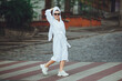 A glamorous lady in a white bathrobe with a white towel on her head and elegant sunglasses is walking along the street of a big city