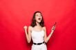 © dianagrytsku - Portrait of young woman screaming and clenching fist like rejoicing victory or triumph isolated over red background