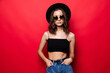 © dianagrytsku - Young pretty woman in floppy hat and sunglasses standing isolated on red background